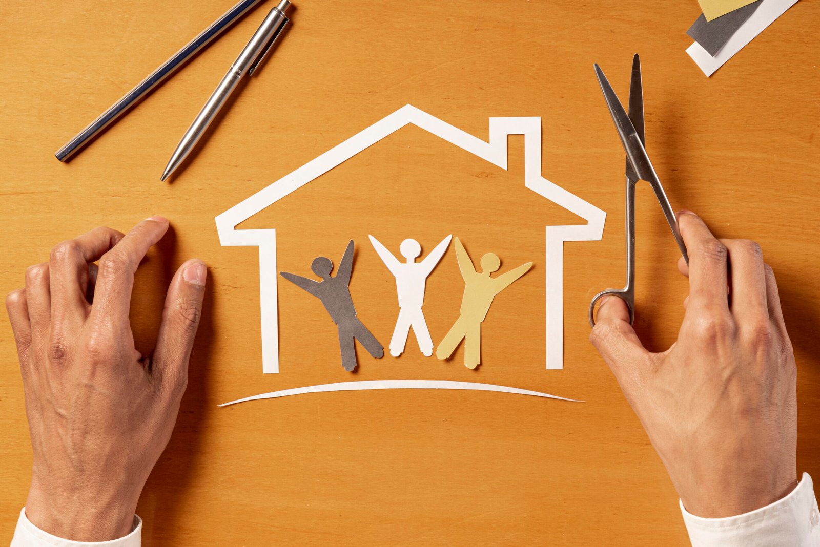 Hands crafting a paper house with family cutouts, symbolizing home and community.