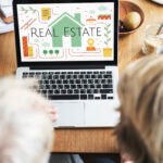 Two people viewing a real estate website with a green house icon on a laptop.