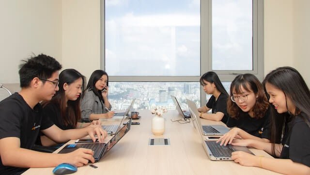 Young professionals collaborating on laptops in a modern office with city view.